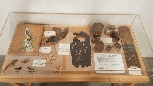 exhibit case containing carved bird pins, painted wood, and polished rocks