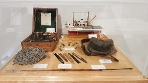 exhibit case containing rope, hat, model boat, fish hooks, sextant